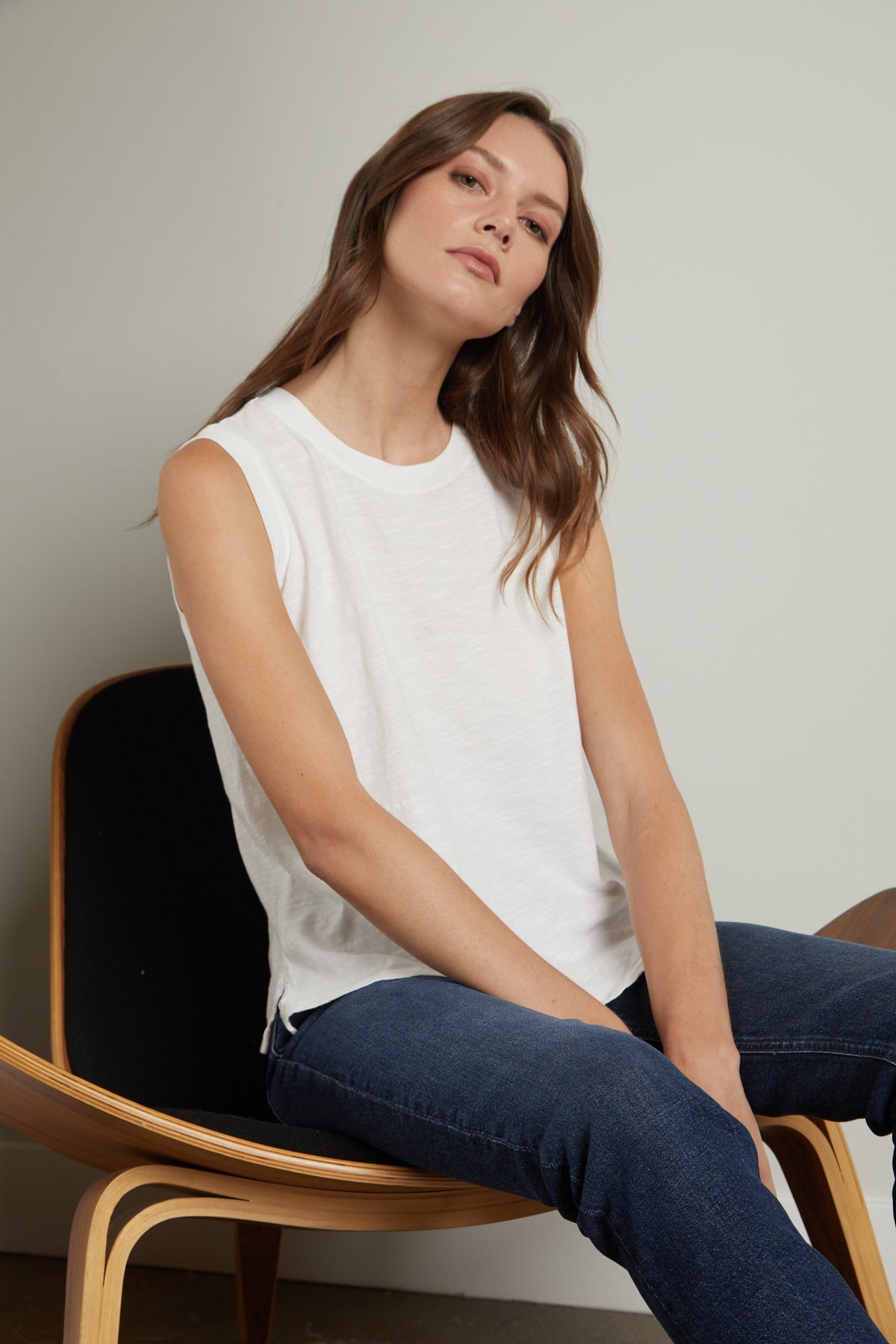   A woman is sitting on a wooden chair wearing jeans and an ELLEN VINTAGE SLUB TANK TOP by Velvet by Graham & Spencer. 