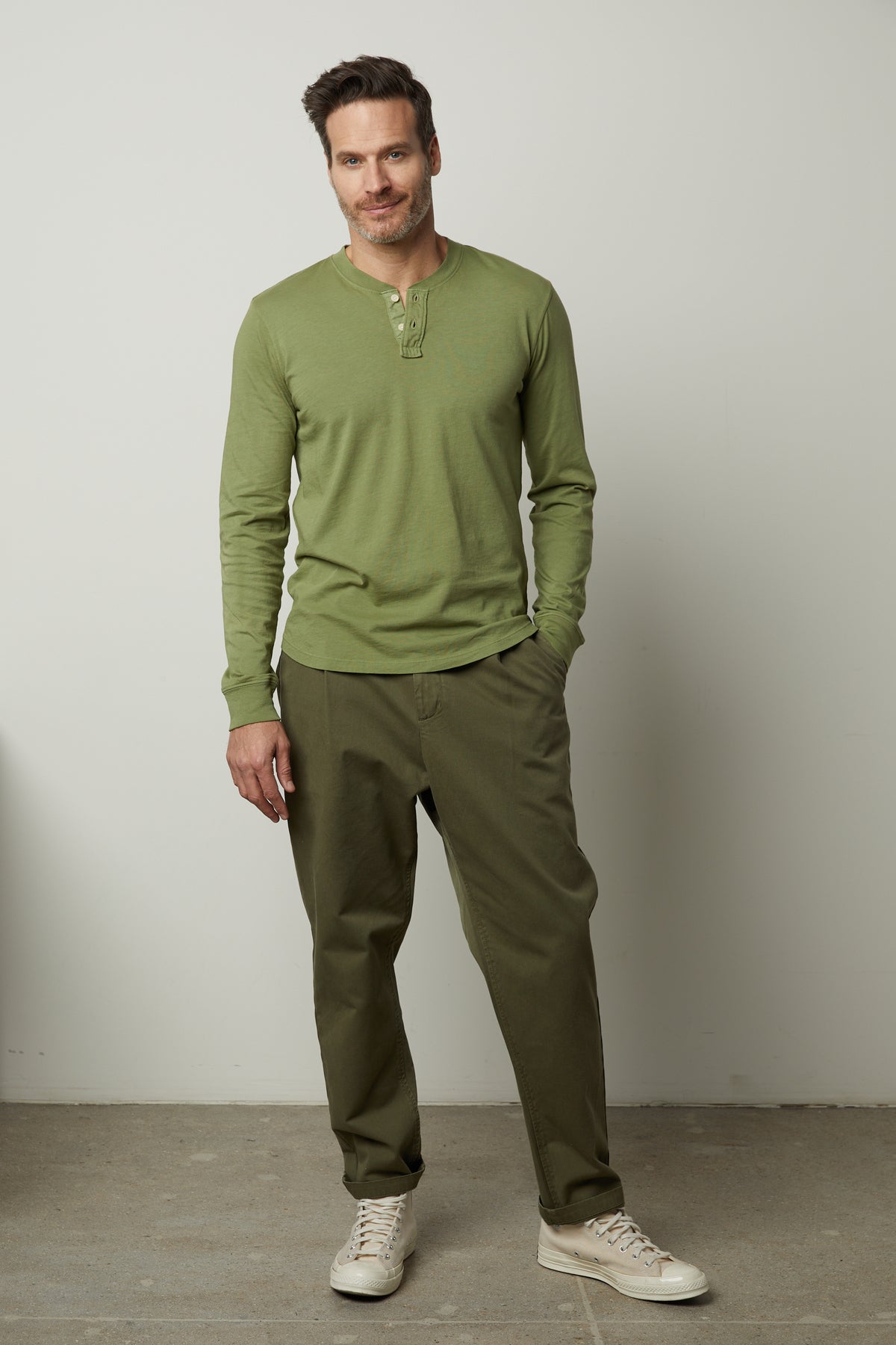   A man wearing a green henley shirt and Velvet by Graham & Spencer khaki pants featuring straight-fit leg and 5 pocket styling. 