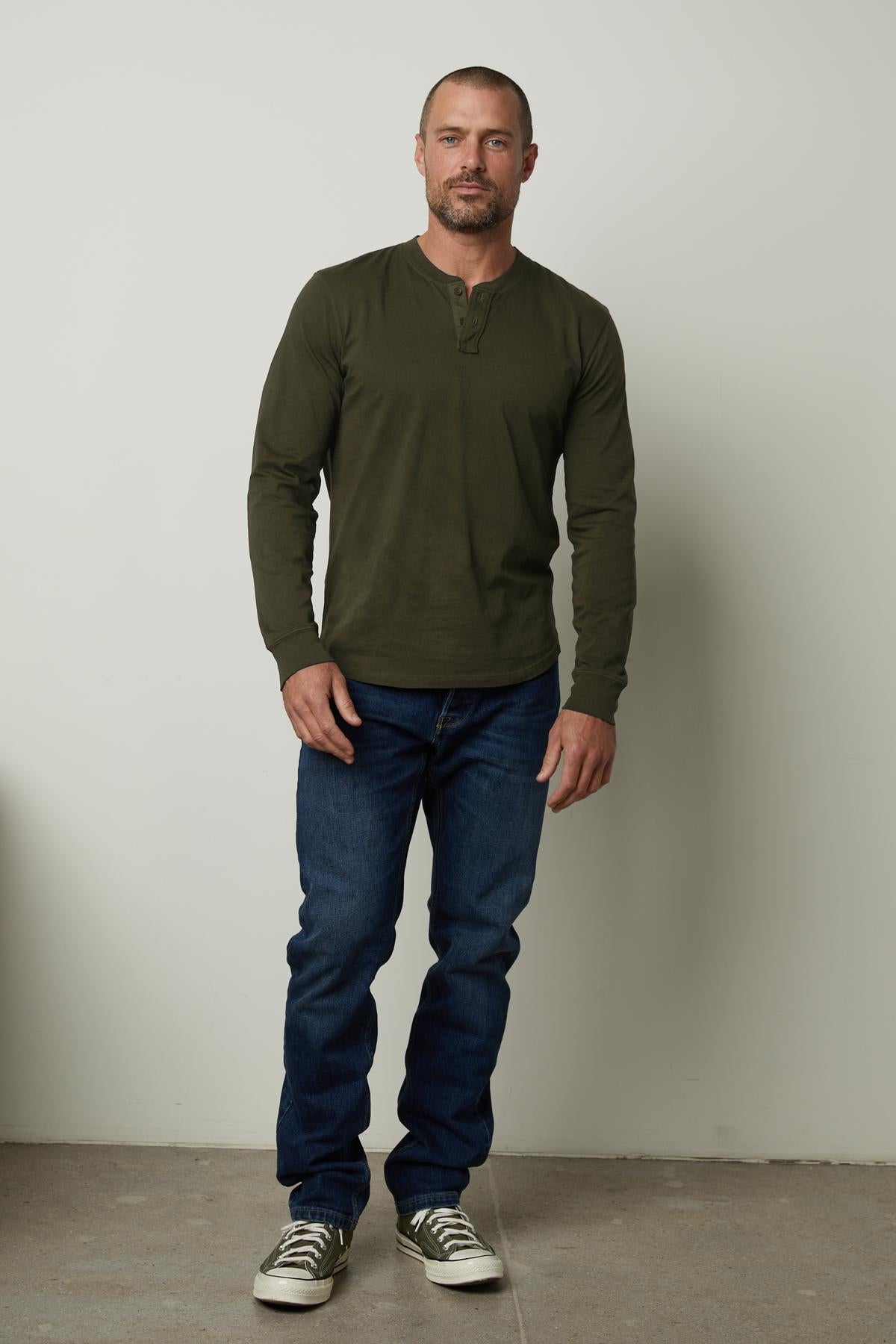 A man wearing a green Velvet by Graham & Spencer Braden Henley shirt made of lightweight cotton fabric and jeans.-35547527151809