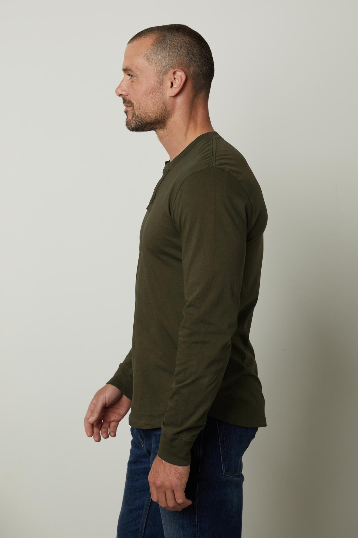 A man wearing a lightweight green Velvet by Graham & Spencer BRADEN HENLEY t-shirt made of cotton fabric and jeans.-35547527086273