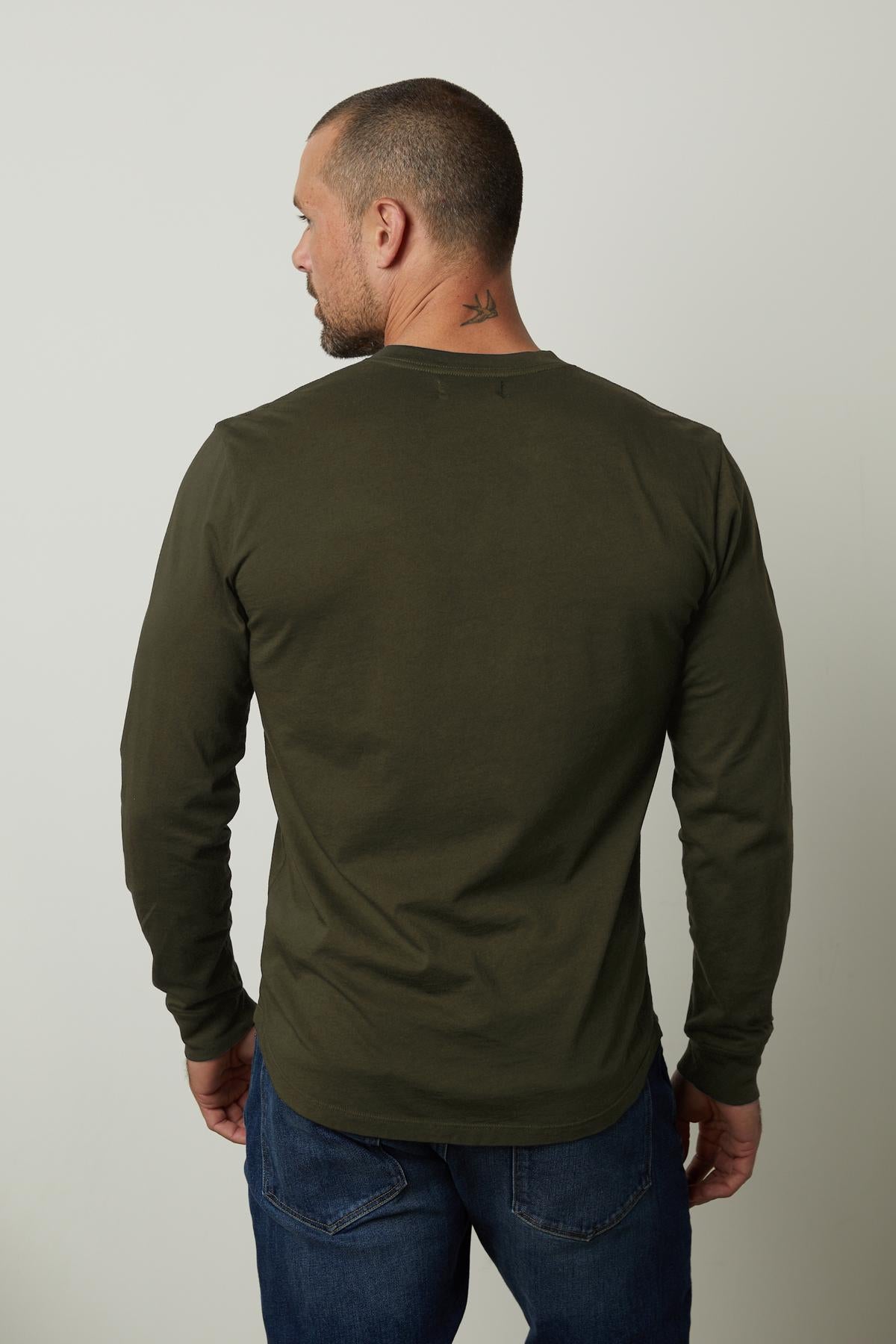   The back view of a man wearing a Velvet by Graham & Spencer lightweight green long sleeve t-shirt made of cotton fabric, called the BRADEN HENLEY. 