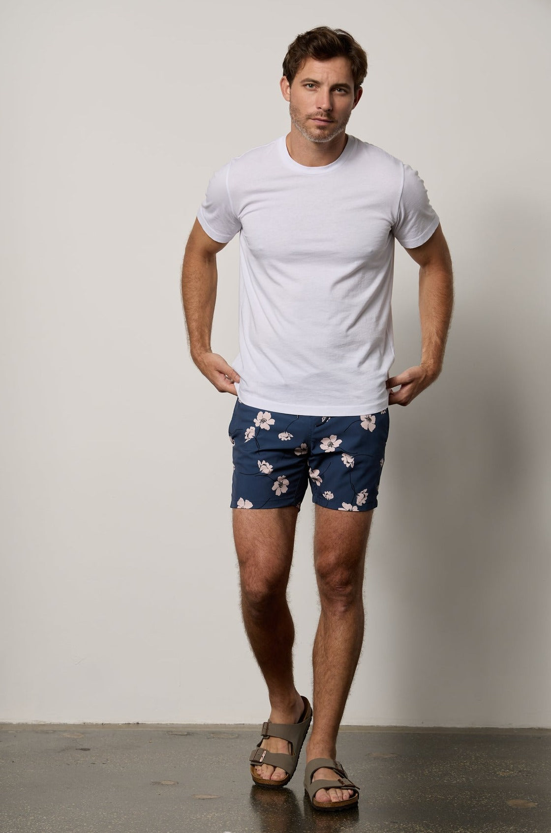   A man wearing a Velvet by Graham & Spencer RICARDO PRINTED SWIM SHORT and a t-shirt, standing in front of a white wall. 
