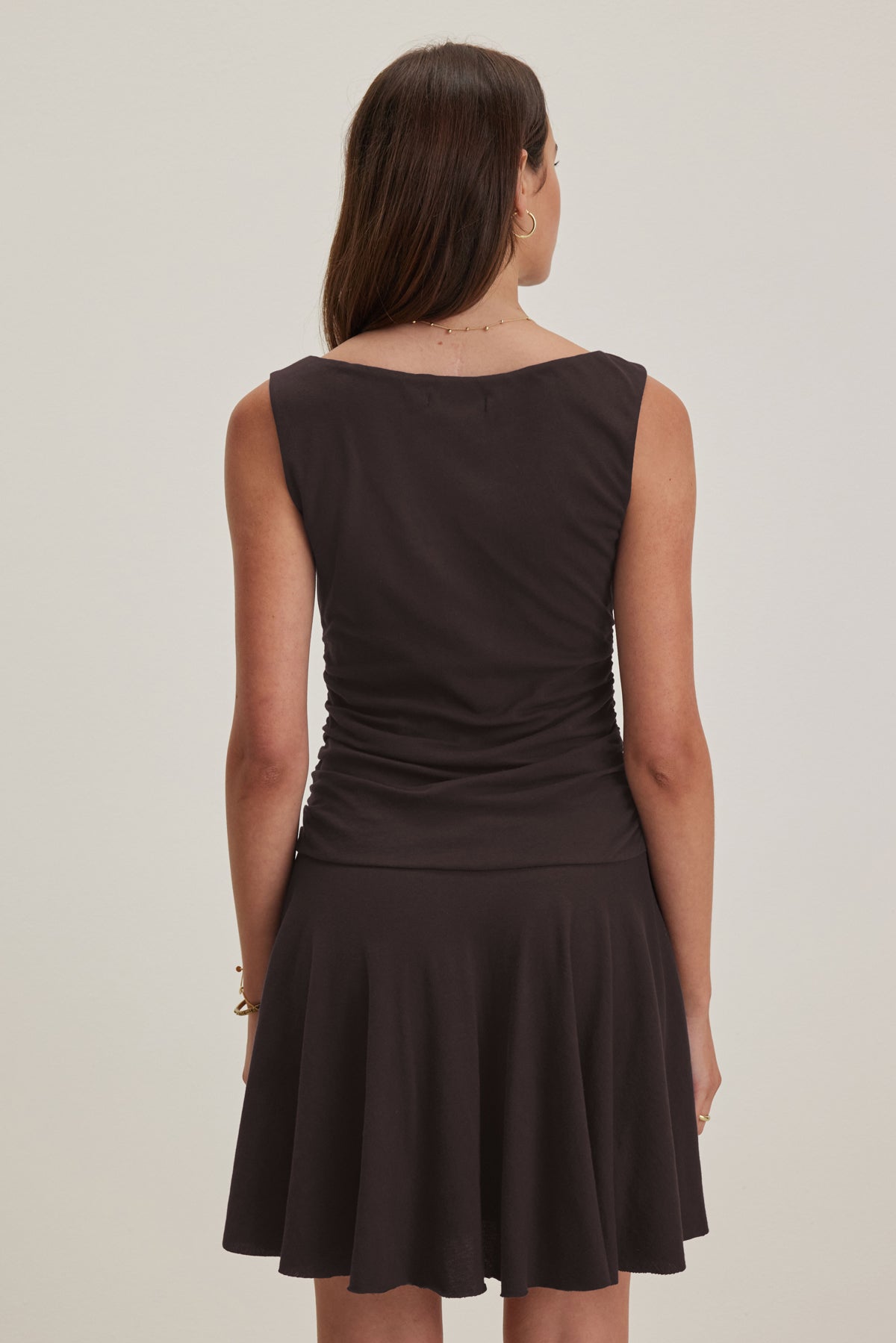   A woman, wearing the sleeveless ALICIA DRESS by Velvet by Graham & Spencer, exudes classic and timeless elegance as she stands with her back to the camera, gazing thoughtfully to the left. 