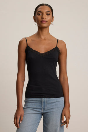 A woman faces forward wearing the INDIE LACE CAMI by Velvet by Graham & Spencer, a black tank top with delicate lace detailing, paired with light blue jeans against a neutral background.