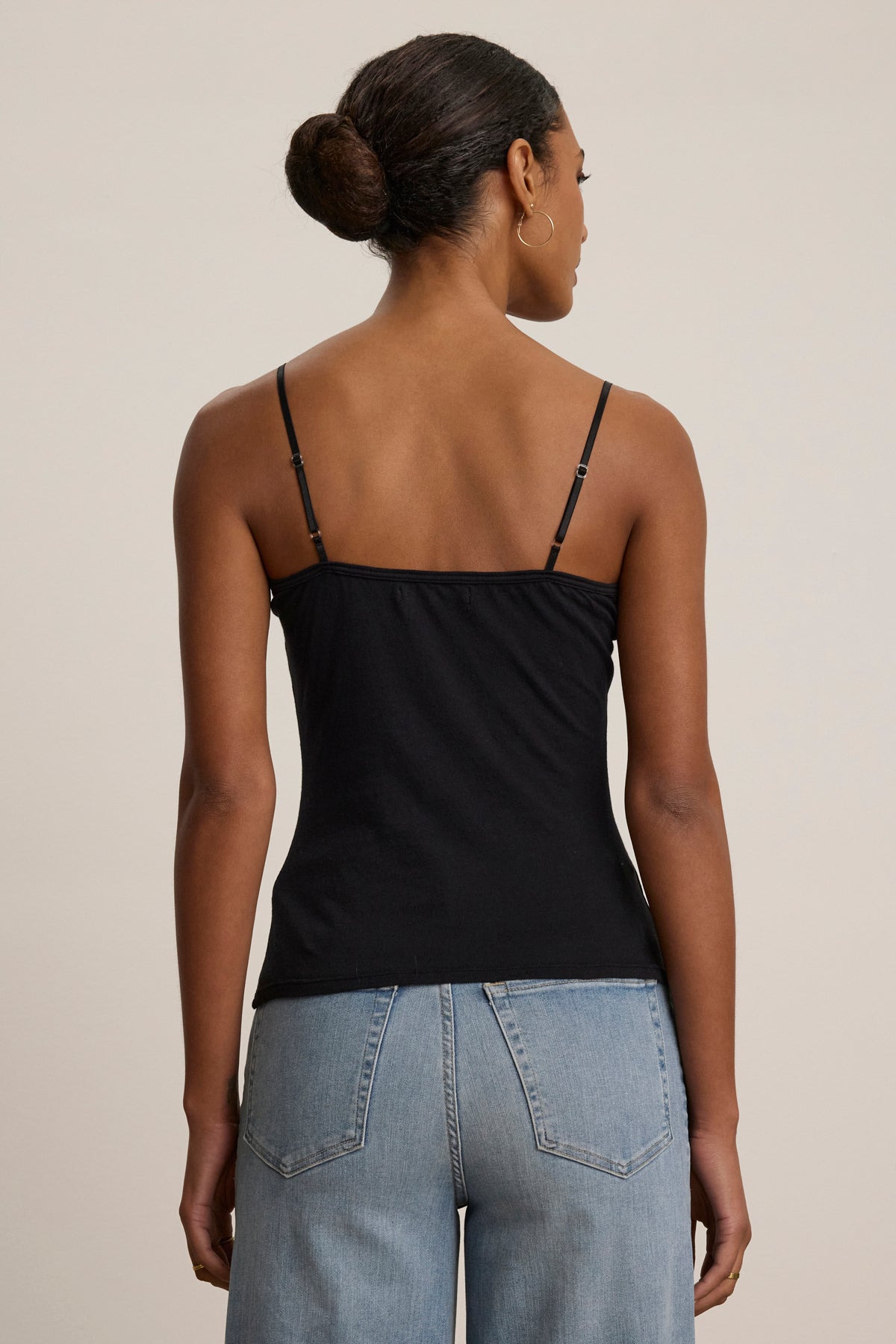 A woman faces away, wearing the Velvet by Graham & Spencer INDIE LACE CAMI with adjustable straps and light blue high-waisted jeans.-39079954677953