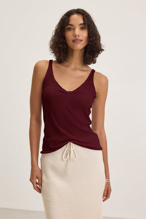 A woman wears the KIM TANK TOP by Velvet by Graham & Spencer—a sleeveless maroon V-neck top—paired with a cream skirt, standing against a plain light background.