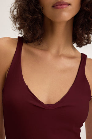 A woman with curly hair models the Velvet by Graham & Spencer KIM TANK TOP, a lightweight cotton essential in deep burgundy. Shown from shoulders to lips, the image highlights the tank’s flattering neckline and sleeveless cut.