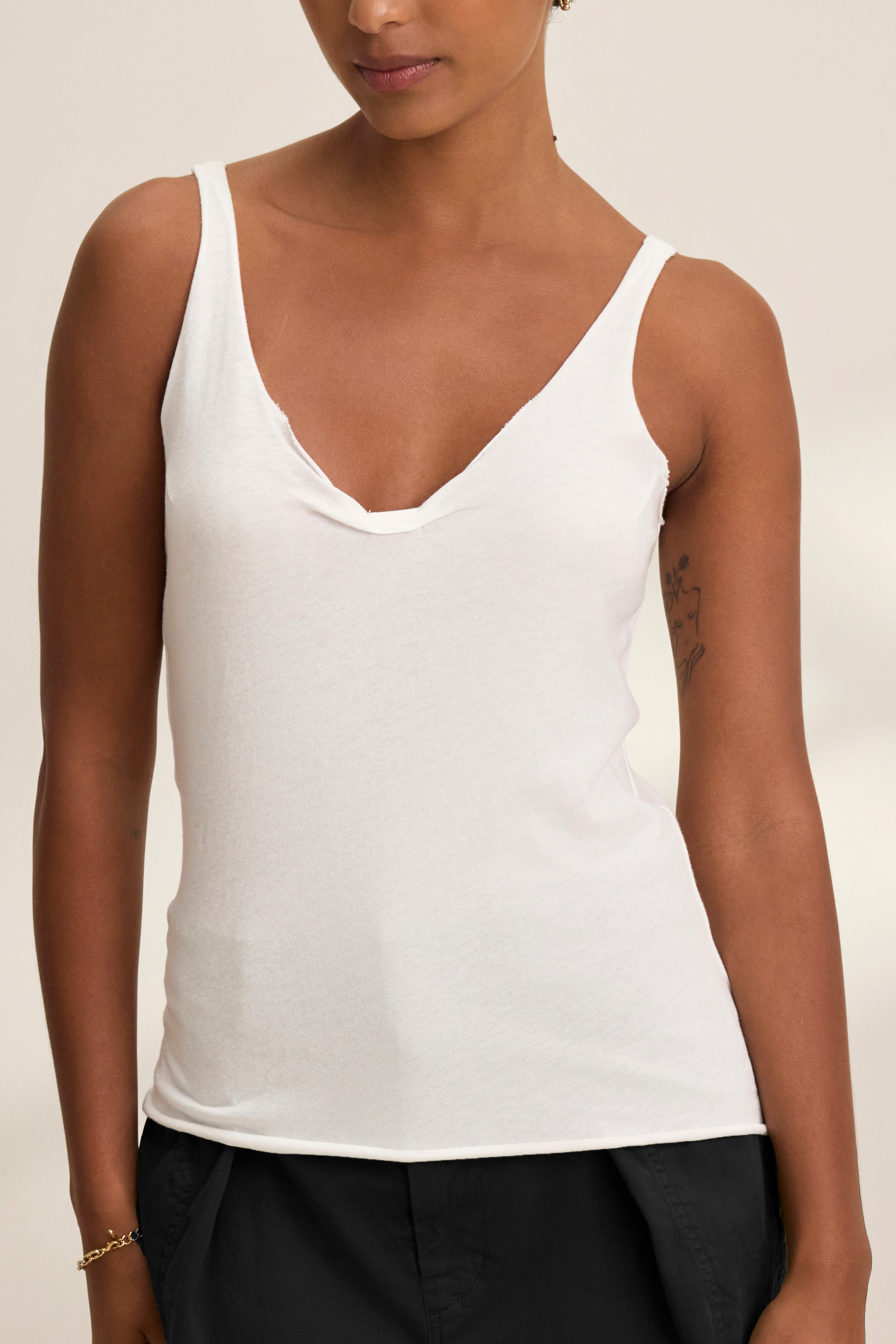   A person wearing the KIM TANK TOP by Velvet by Graham & Spencer—a white lightweight cotton scoop-neck tank—paired with black pants, standing against a neutral background; a true wardrobe essential. 