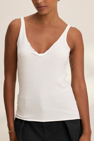 A person wearing the KIM TANK TOP by Velvet by Graham & Spencer—a white lightweight cotton scoop-neck tank—paired with black pants, standing against a neutral background; a true wardrobe essential.