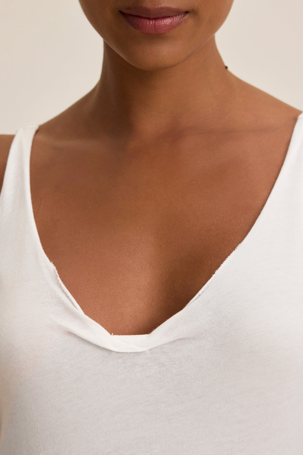 A person with medium skin tone wearing the KIM TANK TOP by Velvet by Graham & Spencer, a classic white V-neck made from lightweight cotton, shown from shoulders to upper chest—a true wardrobe essential.-40010727588033