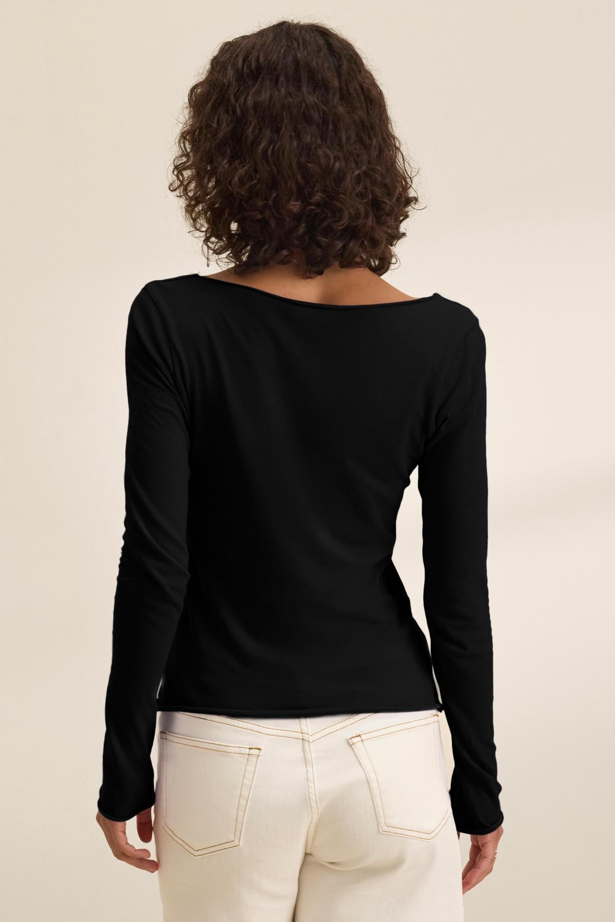 A person with curly brown hair is seen from the back, wearing the NOURA TEE by Velvet by Graham & Spencer and high-waisted off-white jeans against a plain background.-40500868710593