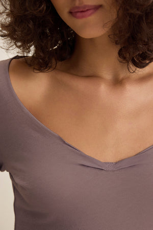 A person with curly brown hair models the NOURA TEE by Velvet by Graham & Spencer—a classic mauve cotton jersey V-neck—shown from shoulders to just above the lips.
