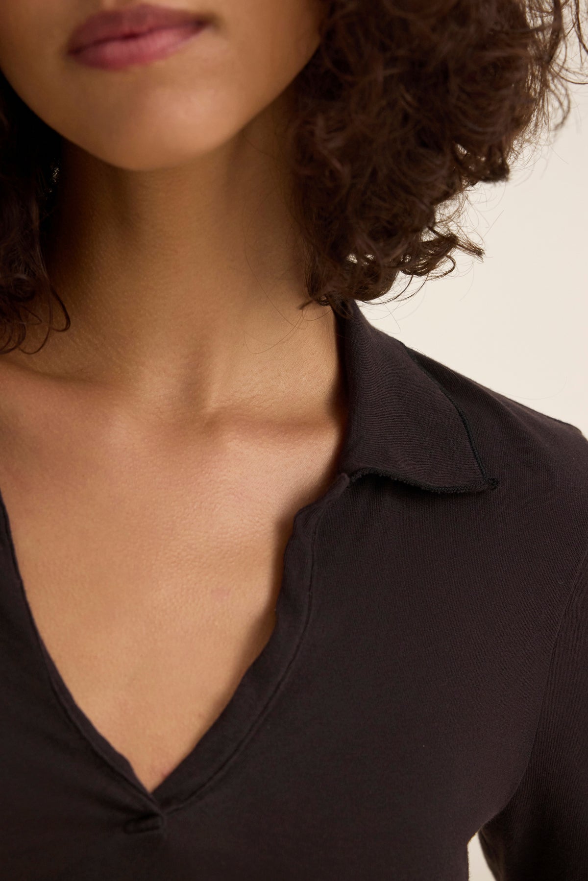 A person wearing the classic REED POLO by Velvet by Graham & Spencer, with curly hair and a partially visible face against a neutral light background.-38928814047425