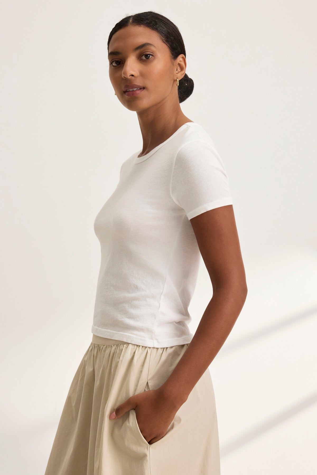 Someone exudes timeless style wearing the WHITNEY TEE by Velvet by Graham & Spencer and beige pants, standing against a light background and gazing confidently at the camera.-38928815489217