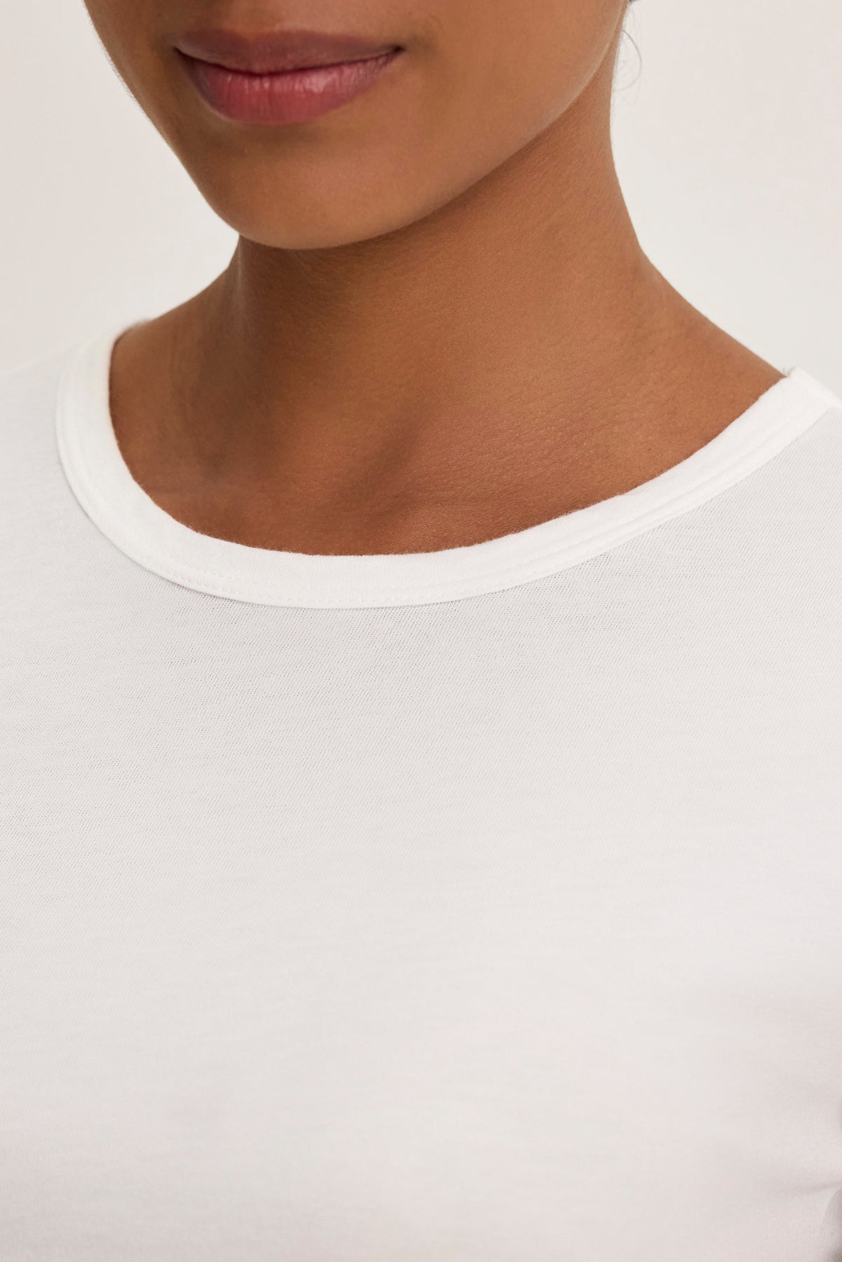 A person wearing the WHITNEY TEE by Velvet by Graham & Spencer exudes timeless elegance against a neutral background, reminiscent of classic style in early collections.-38928815423681
