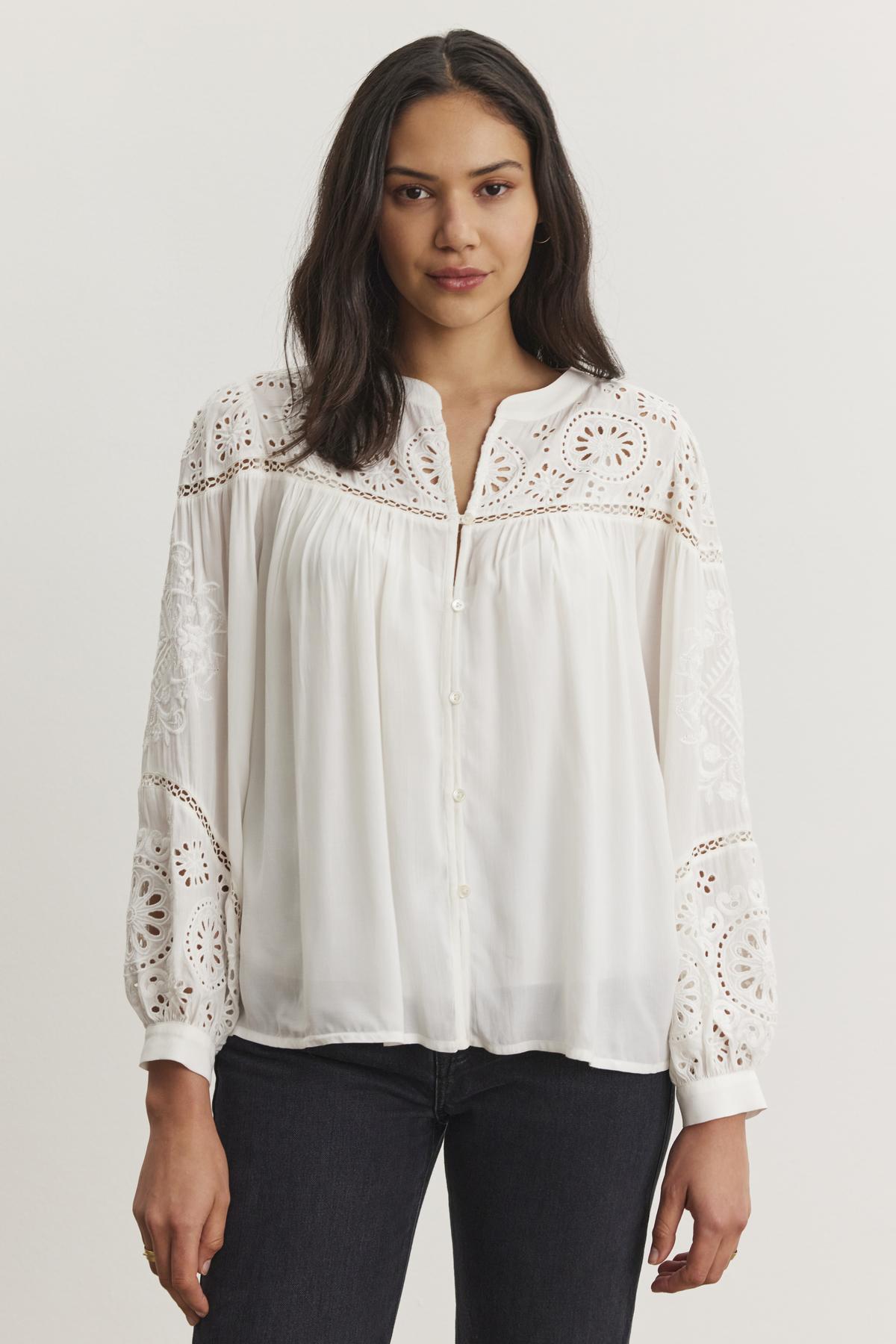   A woman models the LIBBY TOP, a white long-sleeve blouse with lace and eyelet embroidery by Velvet by Graham & Spencer, teamed with dark jeans against a plain background. 