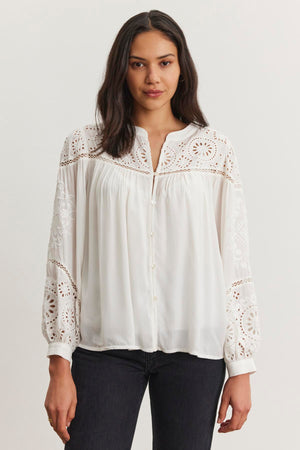 A woman models the LIBBY TOP, a white long-sleeve blouse with lace and eyelet embroidery by Velvet by Graham & Spencer, teamed with dark jeans against a plain background.