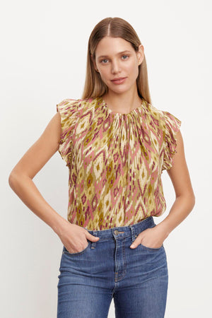 The model is wearing an ADARA PRINTED FLUTTER SLEEVE TOP by Velvet by Graham & Spencer and jeans.