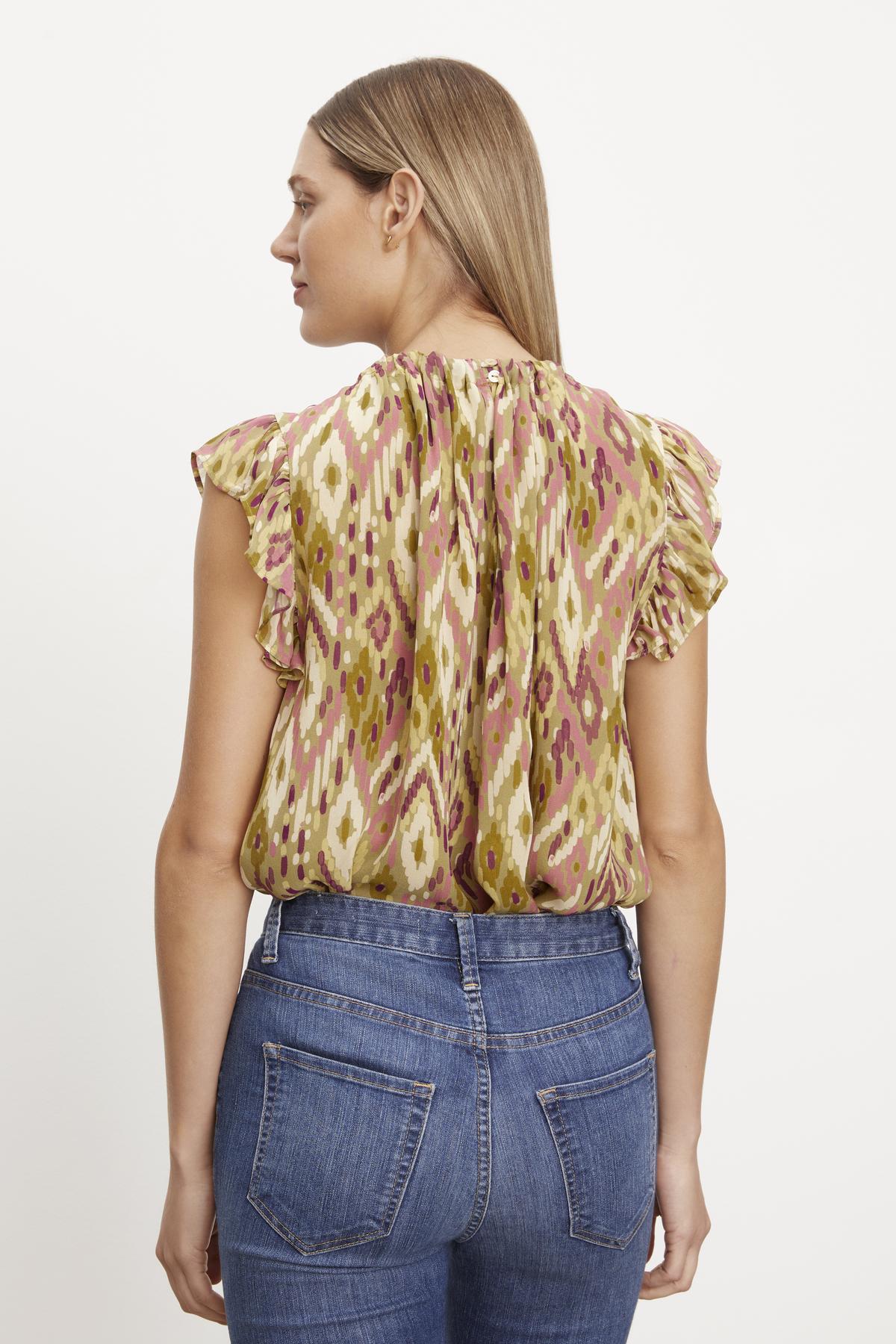   The back view of a woman wearing jeans and an ADARA PRINTED FLUTTER SLEEVE TOP by Velvet by Graham & Spencer. 