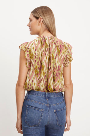The back view of a woman wearing jeans and an ADARA PRINTED FLUTTER SLEEVE TOP by Velvet by Graham & Spencer.