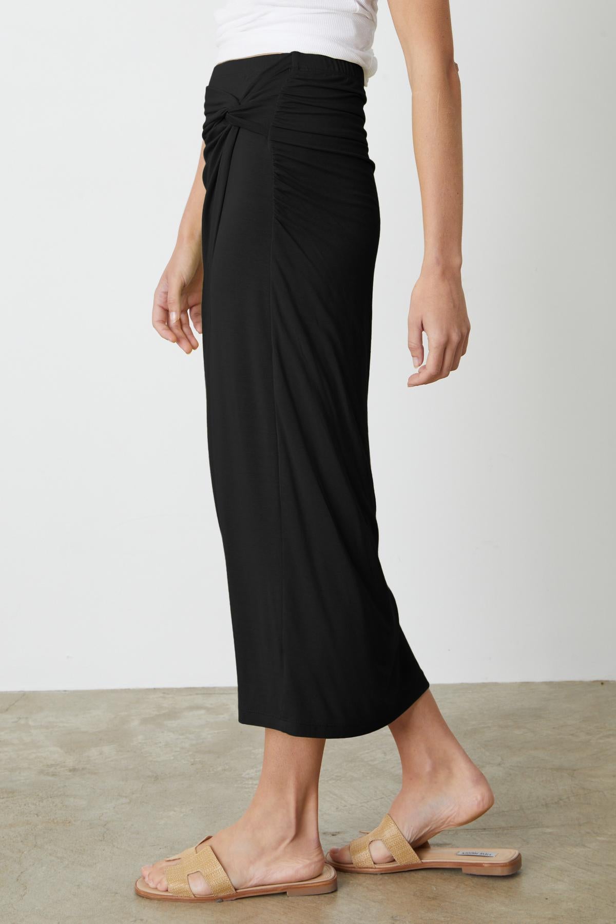 A woman wearing a Velvet by Graham & Spencer SHAE TWIST FRONT SKIRT and sandals.-35201185120449