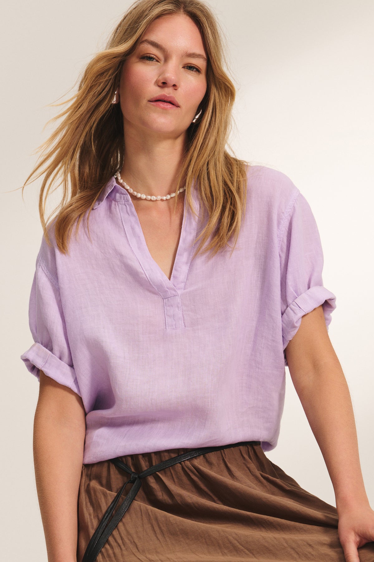 A woman wearing the VIVICA LINEN TOP by Velvet by Graham & Spencer, paired with a brown skirt, black belt, and pearl necklace stands against a neutral background.-39173165351105