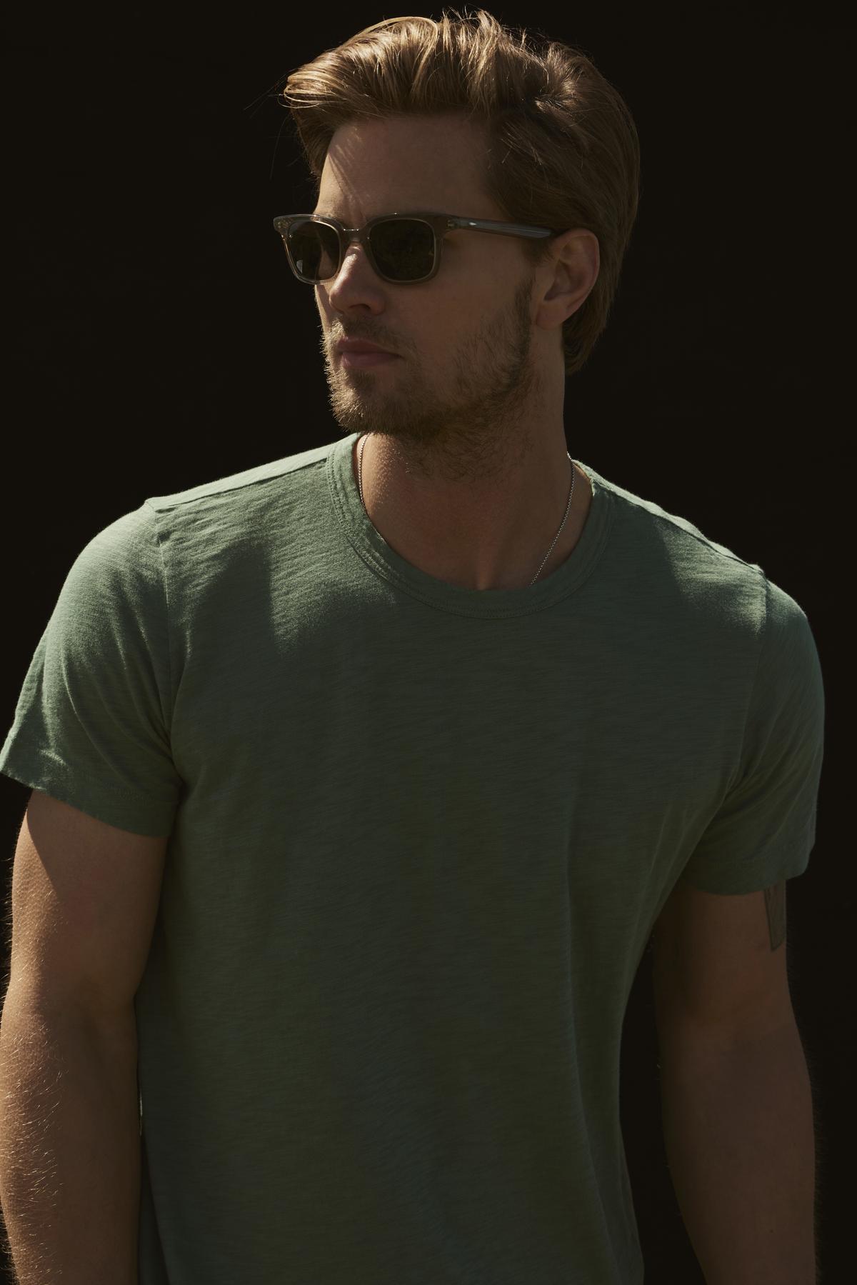 A man in a Velvet by Graham & Spencer SAMSEN WHISPER CLASSIC V-NECK TEE and sunglasses, looking to the side against a dark background.-36640154157249