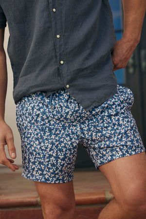 Man wearing a gray shirt tucked into Velvet by Graham & Spencer RICARDO SWIM SHORT, standing with his hand resting on his hip.