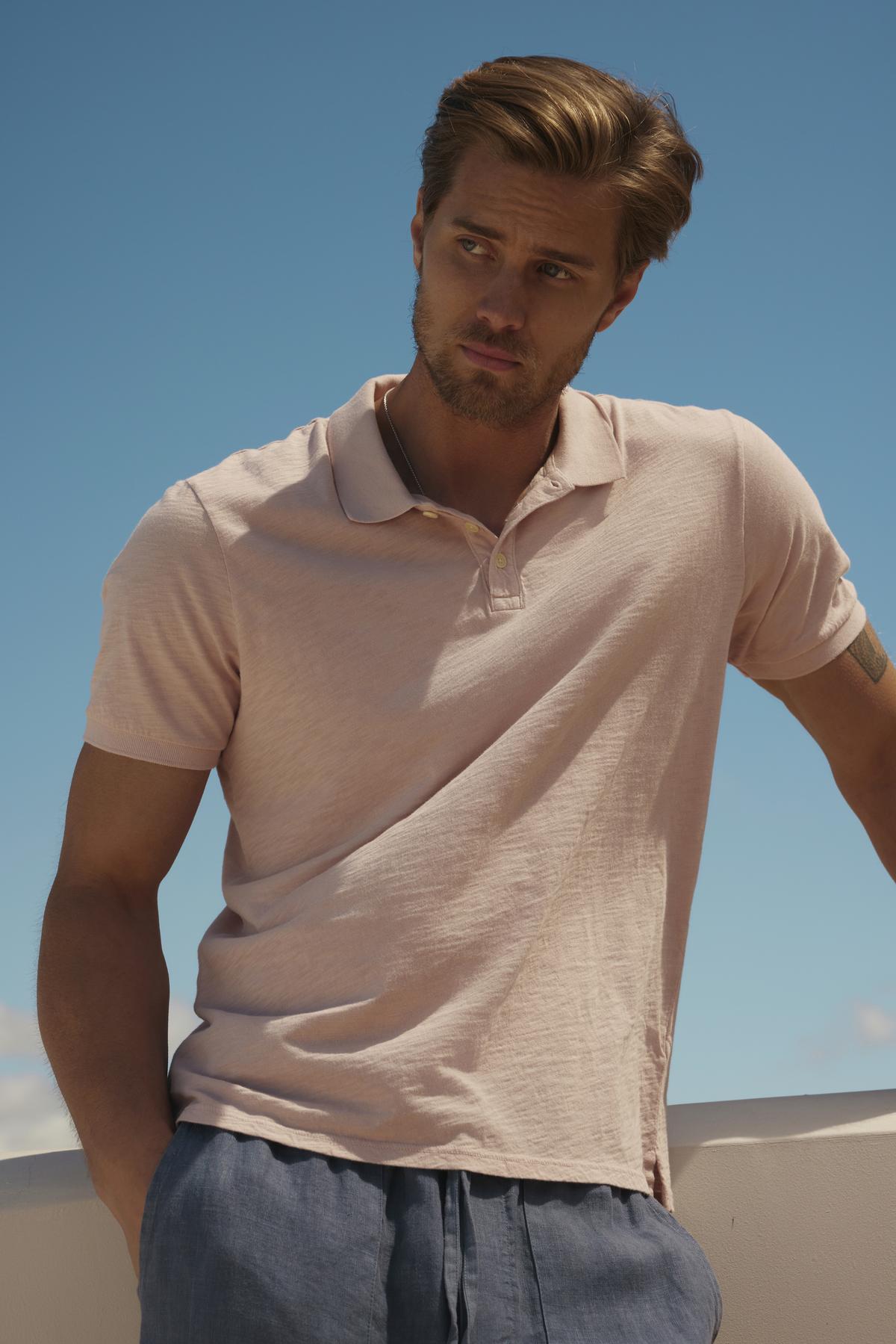 Man in a Velvet by Graham & Spencer NIKO POLO shirt and blue pants standing outdoors, looking away thoughtfully under a clear blue sky.-36753554538689