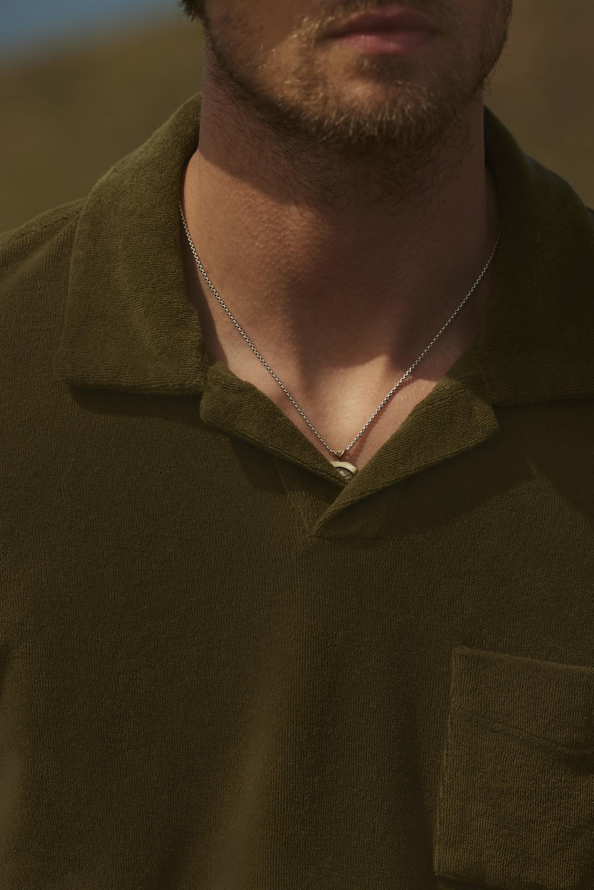 Close-up of a man in a green shirt, focusing on his neck and lower face, with a SERGEY POLO chain visible around his neck. The background is softly blurred.-36753587896513