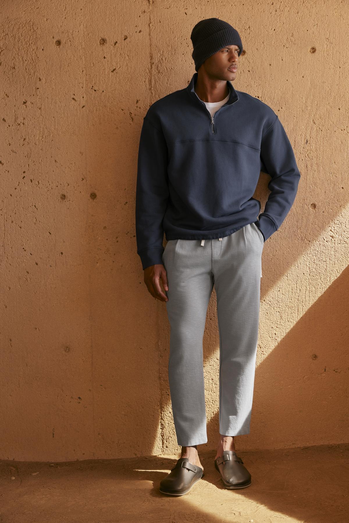   A man is leaning against a wall wearing a Velvet by Graham & Spencer BOSCO QUARTER-ZIP SWEATSHIRT. 