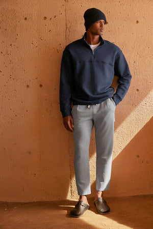 A man is leaning against a wall wearing a Velvet by Graham & Spencer BOSCO QUARTER-ZIP SWEATSHIRT.