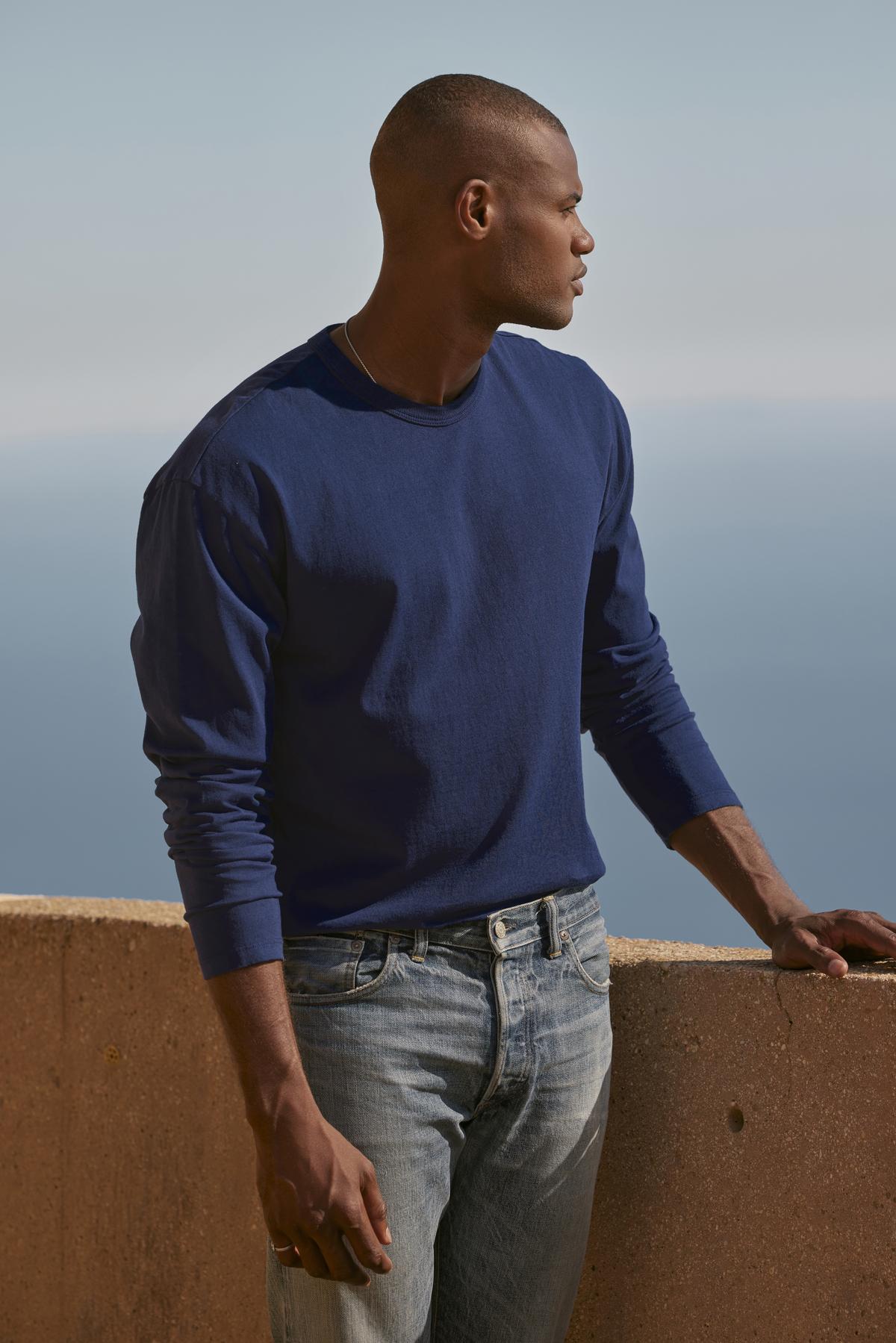   A man in an EDWARD CREW NECK TEE sweatshirt, made of cotton jersey, standing on a ledge overlooking the ocean. (Brand: Velvet by Graham & Spencer) 