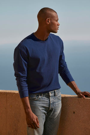 A man in an EDWARD CREW NECK TEE sweatshirt, made of cotton jersey, standing on a ledge overlooking the ocean. (Brand: Velvet by Graham & Spencer)