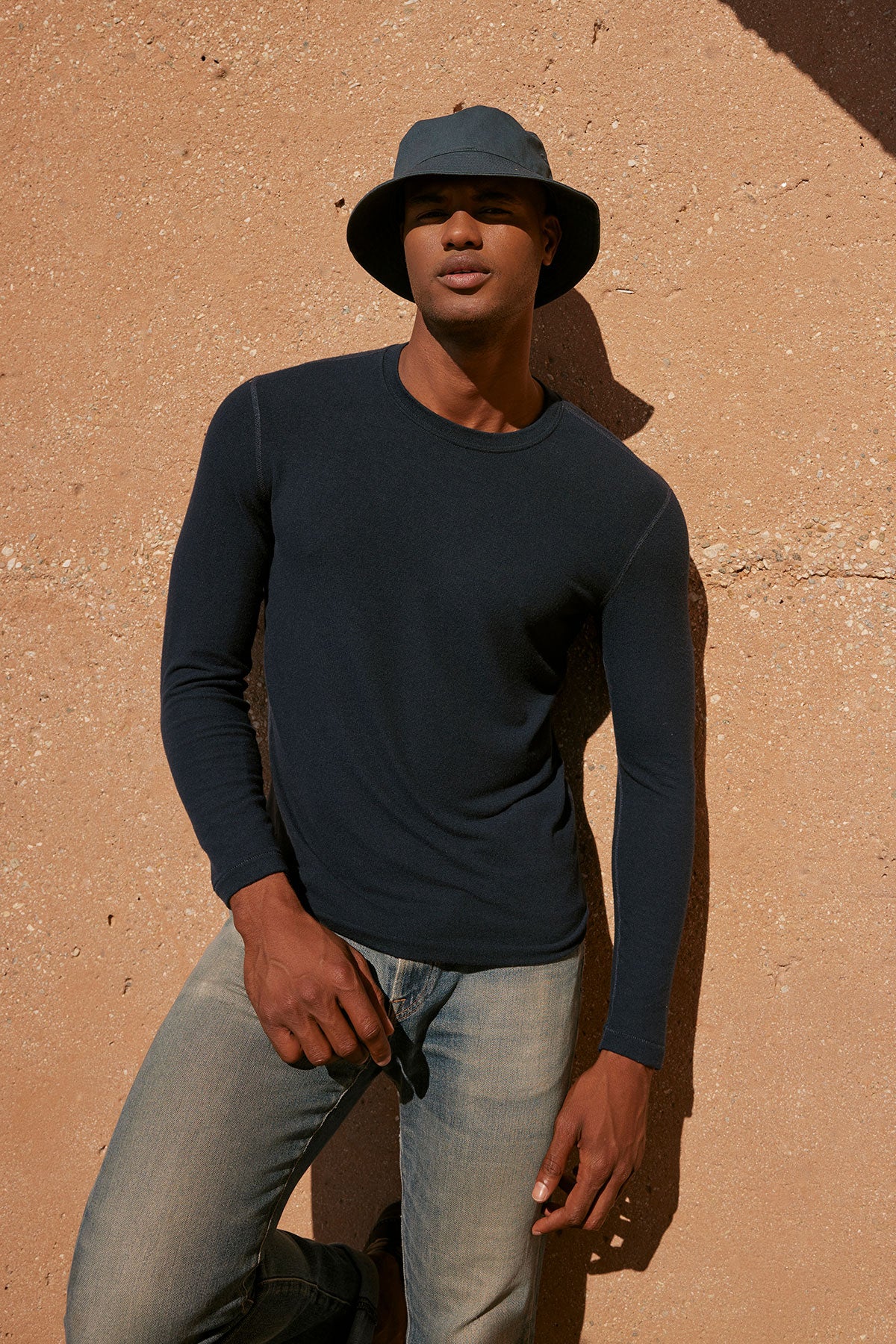 A man in a Velvet by Graham & Spencer BECKER COZY JERSEY CREW hat leaning against a wall.-35678448877761