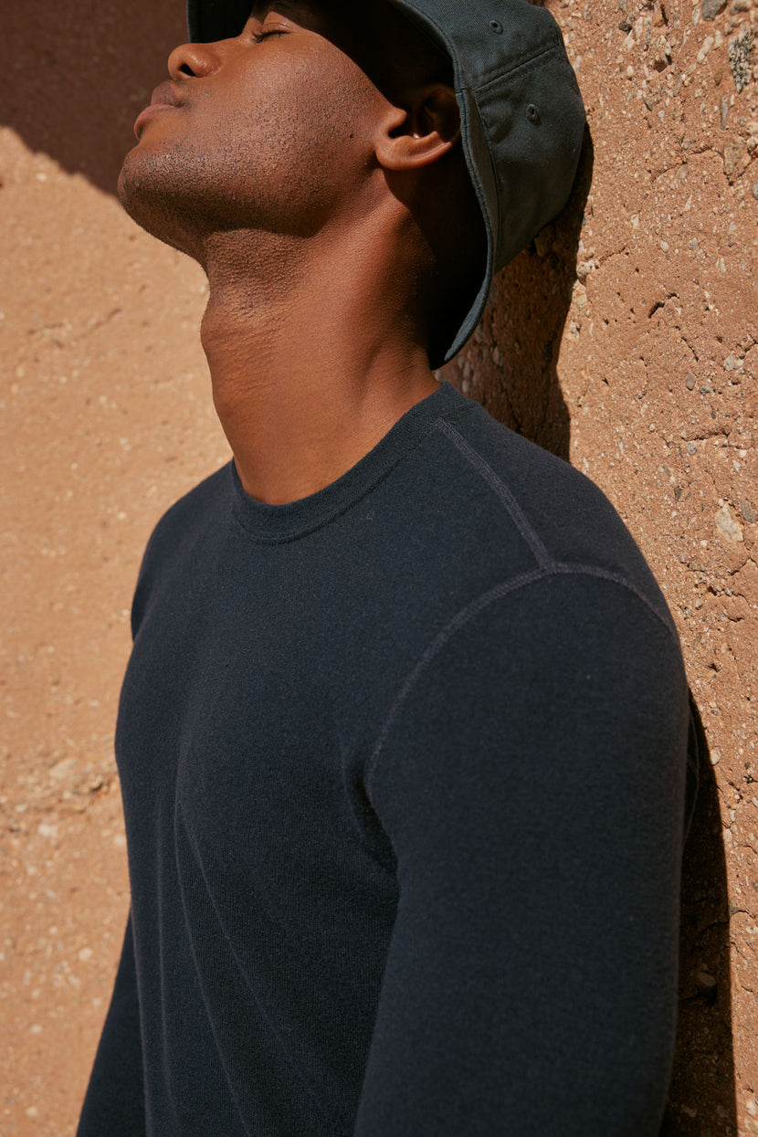 A man wearing a Velvet by Graham & Spencer BECKER COZY JERSEY CREW hat leaning against a wall.