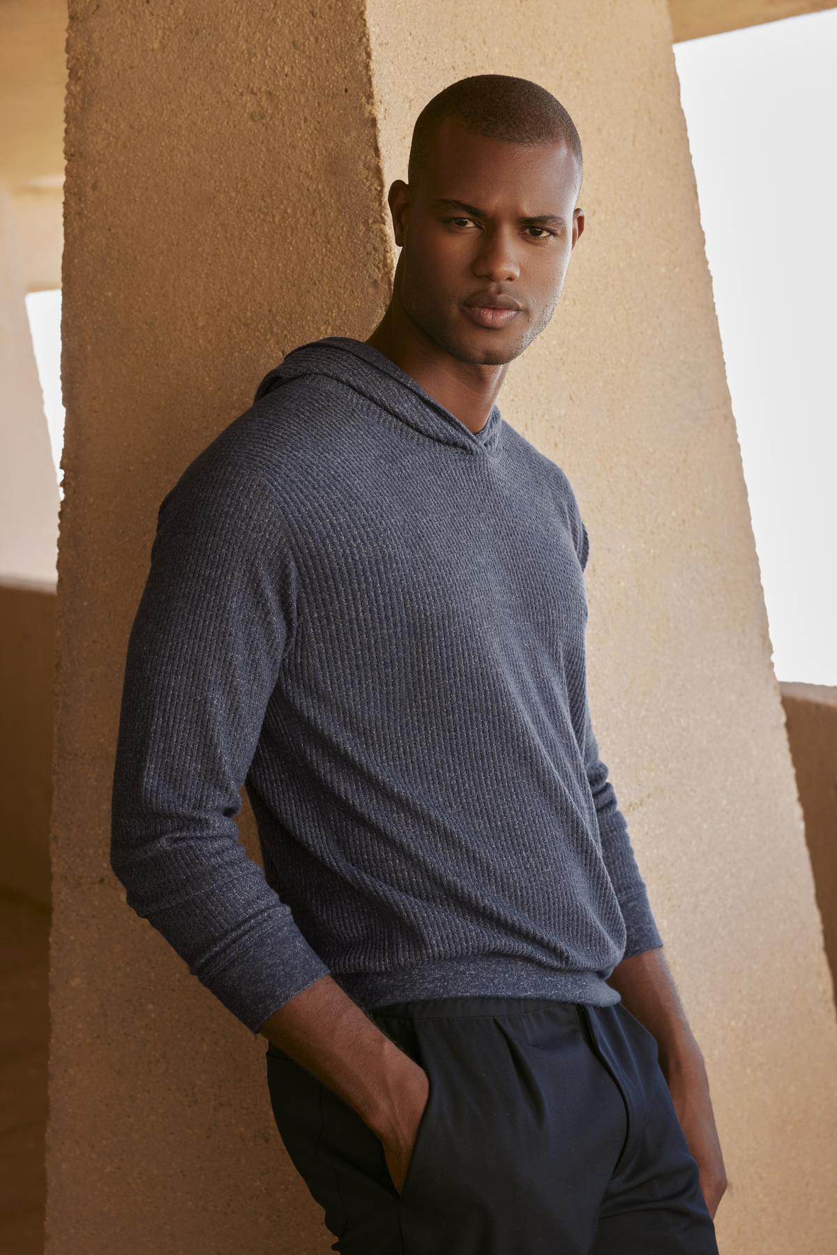   A black man in a Velvet by Graham & Spencer Colin Thermal Hoodie leaning against a wall. 