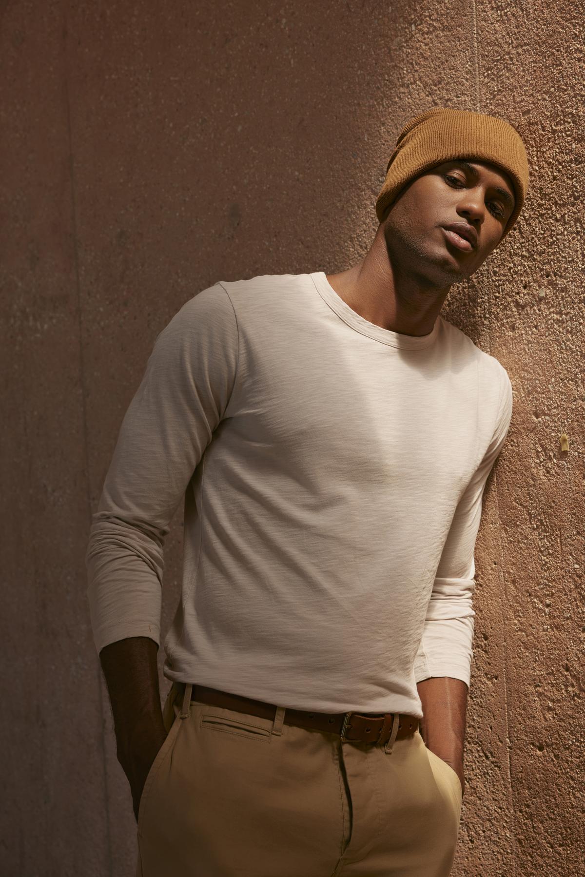 A man wearing a beanie, leaning against a wall, with a vintage-feel texture was wearing the KAI CREW NECK TEE by Velvet by Graham & Spencer.-35547537965249