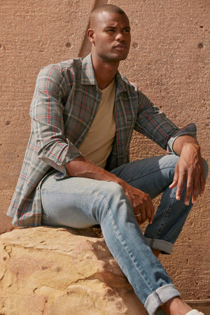 A man sitting on a rock, wearing Velvet by Graham & Spencer's WILDER PLAID BUTTON-UP SHIRT, made with lightweight cotton woven fabric.