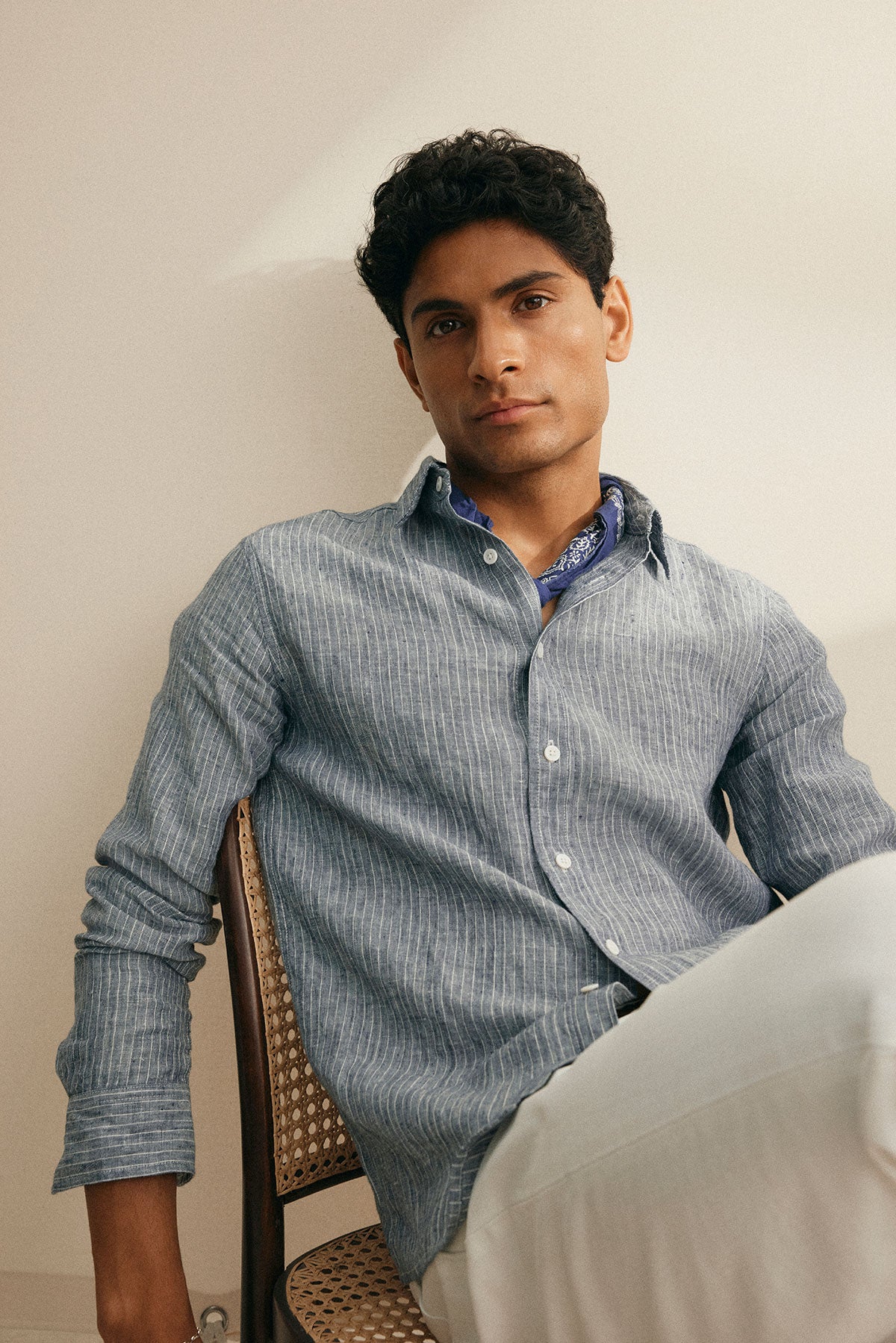   A person in a CARUSO LINEN BUTTON-UP SHIRT by Velvet by Graham & Spencer sits, looking at the camera with a neutral expression, showcasing its versatile design. 