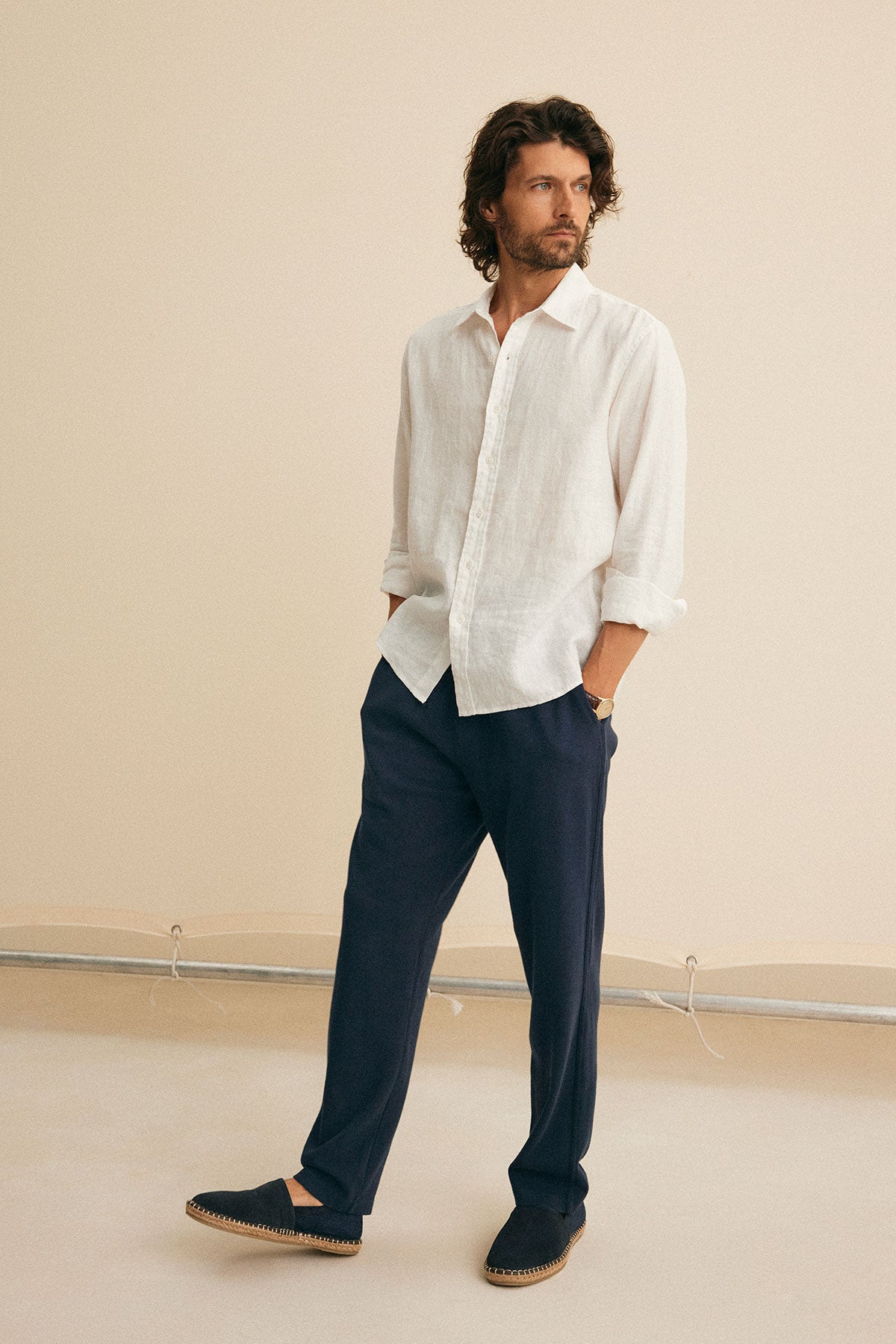   A man wearing the CARUSO LINEN BUTTON-UP SHIRT from Velvet by Graham & Spencer, paired with navy pants and espadrilles, stands against a neutral background, gazing to the side. 