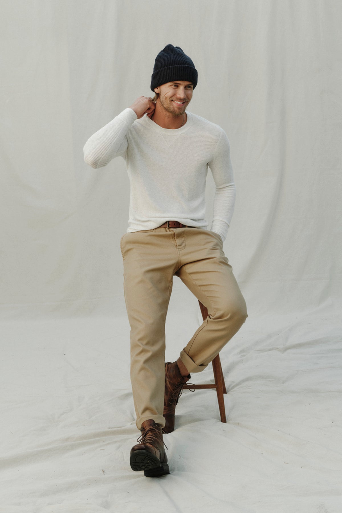  A man sitting on a stool wearing a Velvet by Graham & Spencer AUGUSTUS RIB KNIT CREW beanie and khaki pants. 