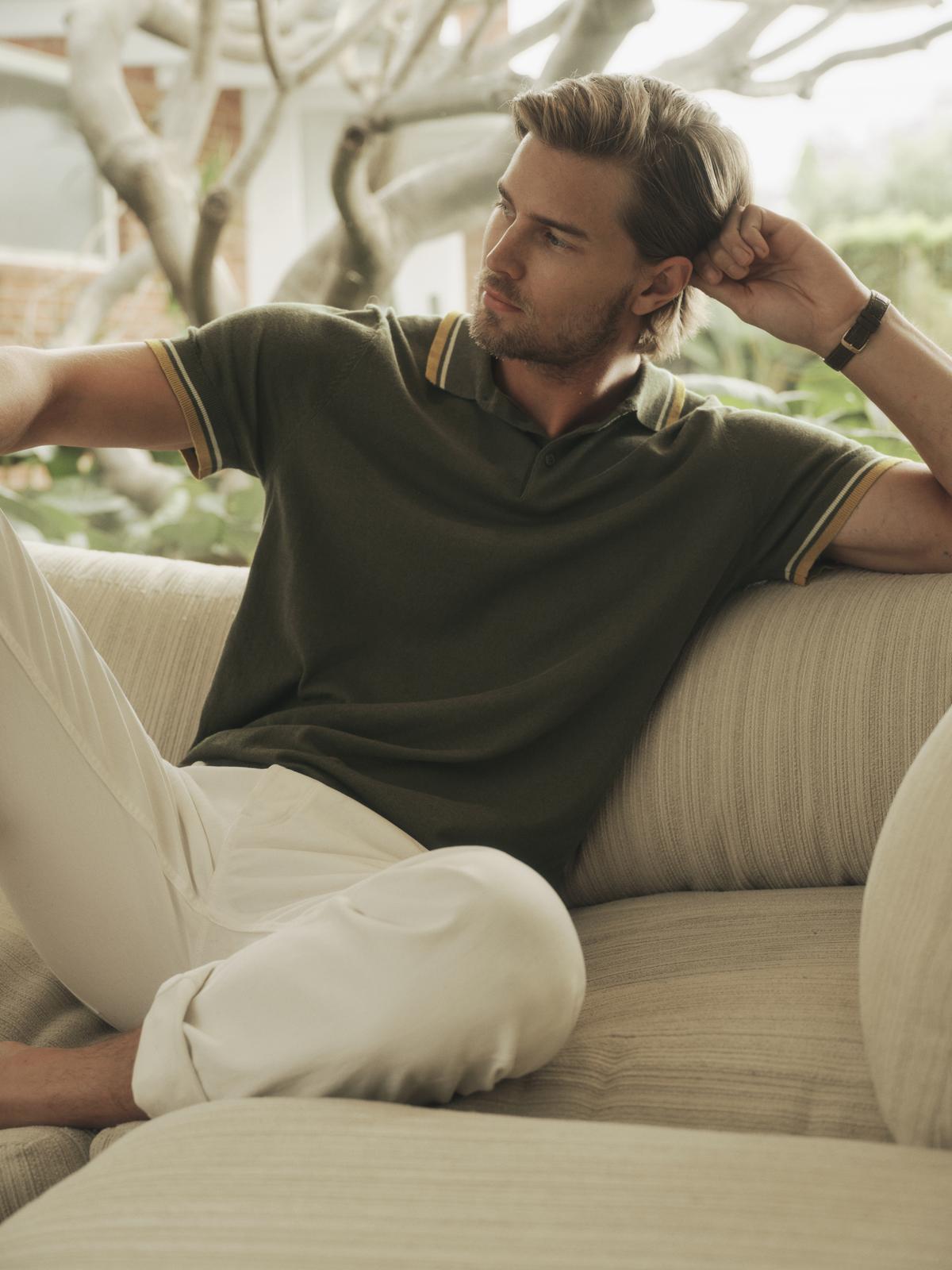   A man sitting on a couch wearing a green Velvet by Graham & Spencer GREGAN LINEN BLEND POLO shirt and white pants. 