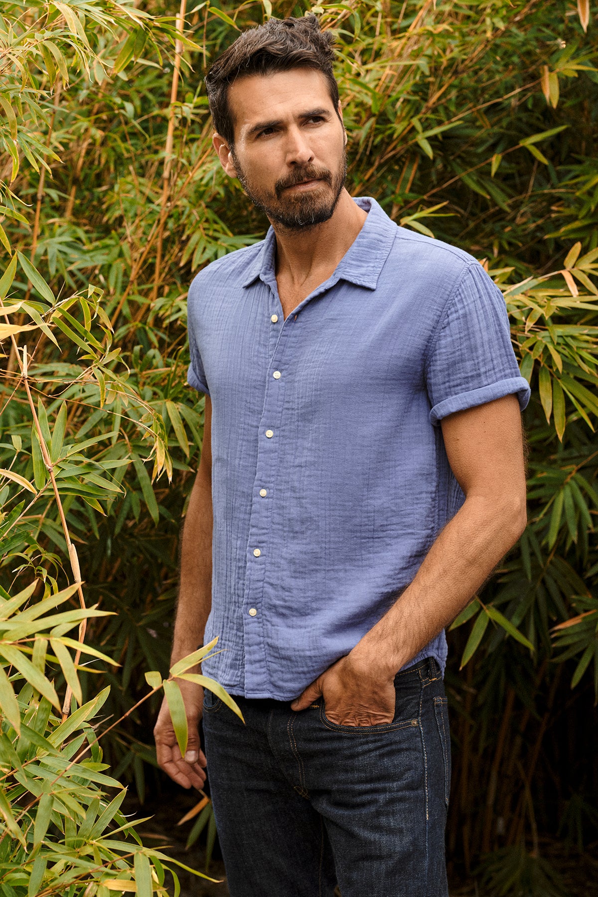   Christian Shirt in citadel blue with dark blue denim, model standing outside near green bamboo with hand in jeans pocket 
