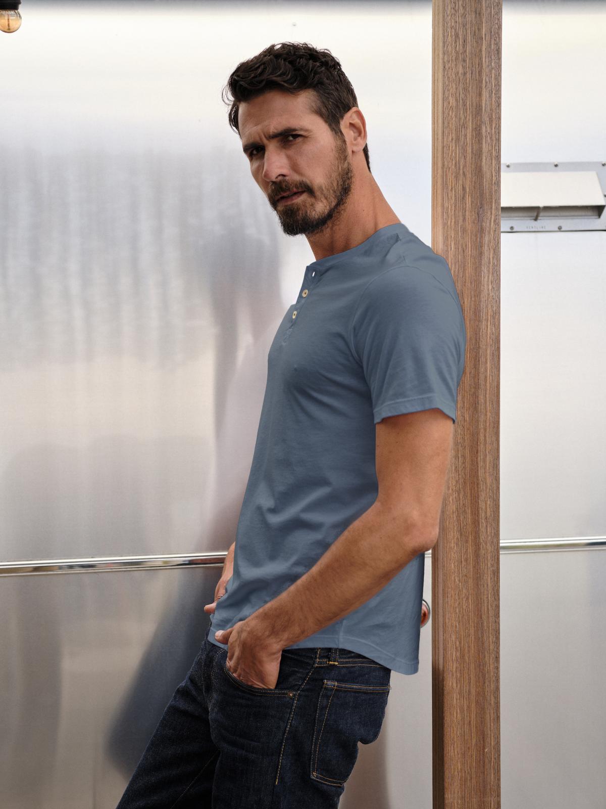   A man leaning against a wall in a Velvet by Graham & Spencer FULTON SHORT SLEEVE HENLEY t-shirt. 