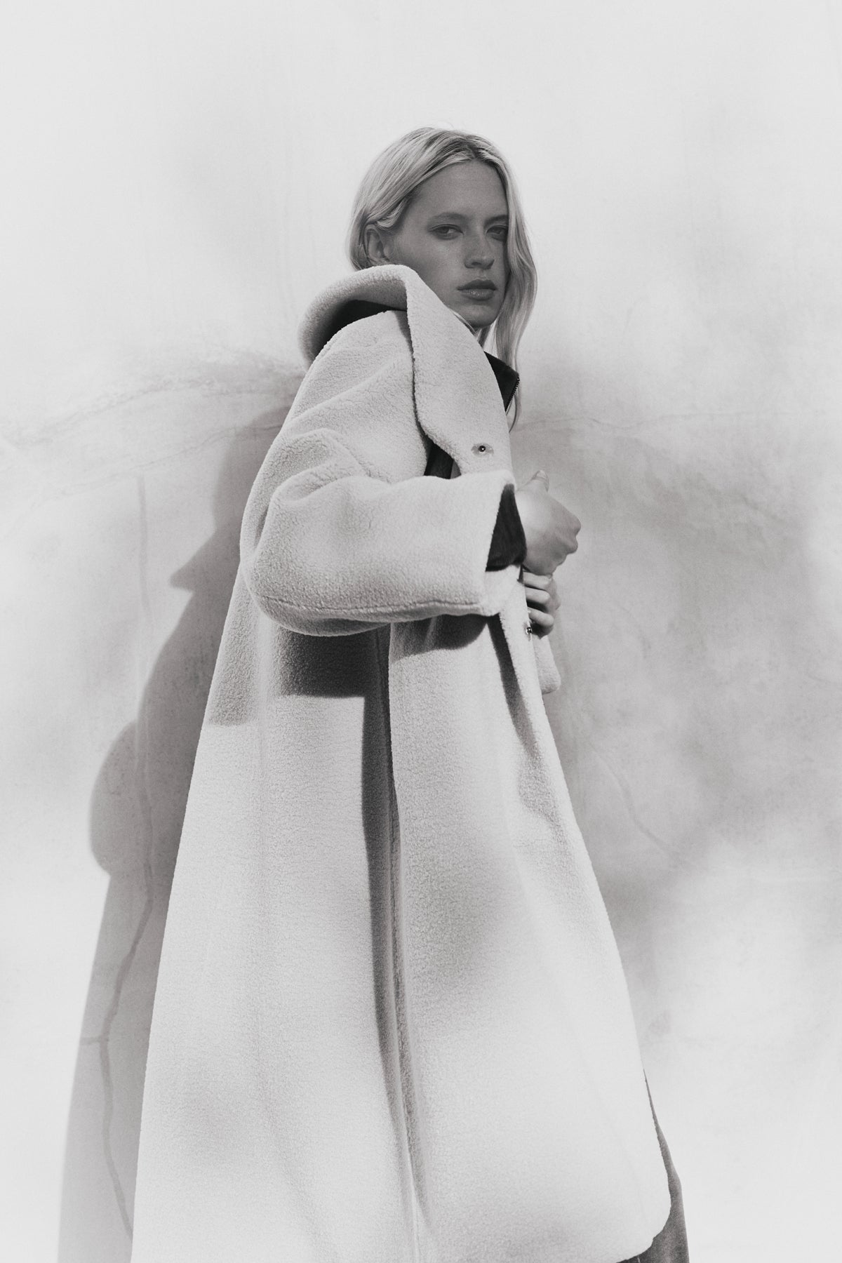 A person models the ELEANOR SHERPA REVERSIBLE COAT by Velvet by Graham & Spencer, standing against a plain, slightly shadowed wall and looking towards the camera.-39838347919553