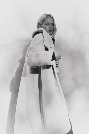 A person models the ELEANOR SHERPA REVERSIBLE COAT by Velvet by Graham & Spencer, standing against a plain, slightly shadowed wall and looking towards the camera.