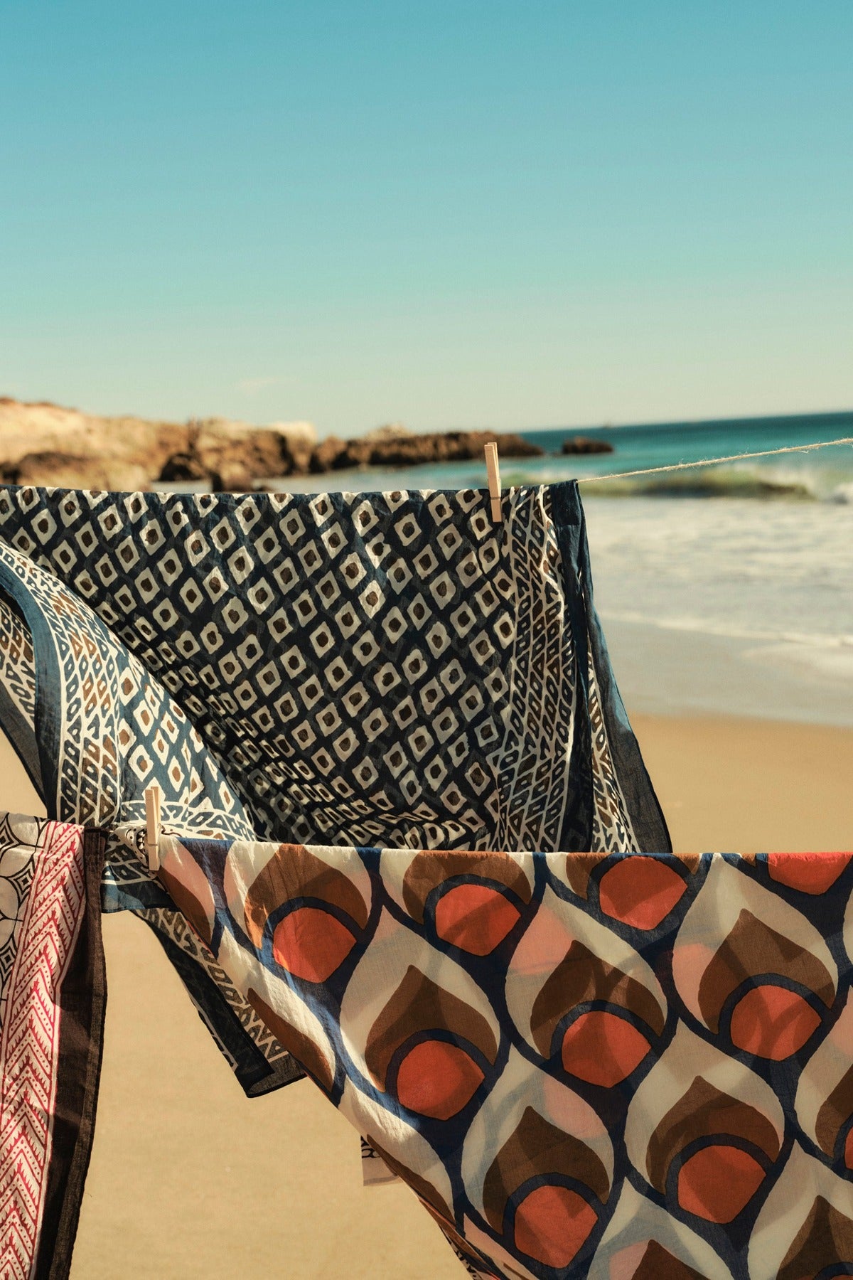   Patterned Velvet by Graham & Spencer SARONG WRAP facing the ocean with waves crashing and rocks in the distance, under a clear blue sky. 