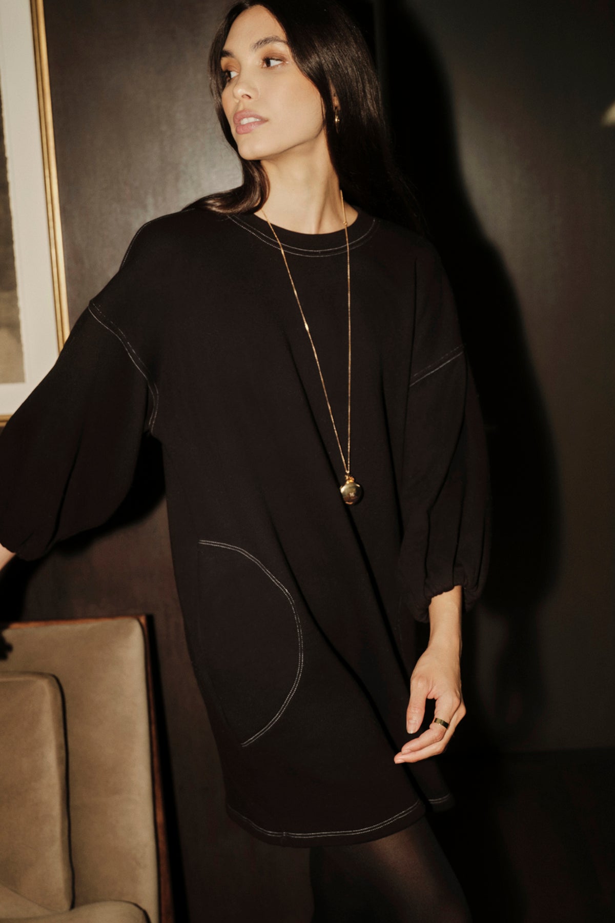 A woman in a comfortable black Velvet by Graham & Spencer Jensen Puff Sleeve Dress leaning against a couch.-35416309137601