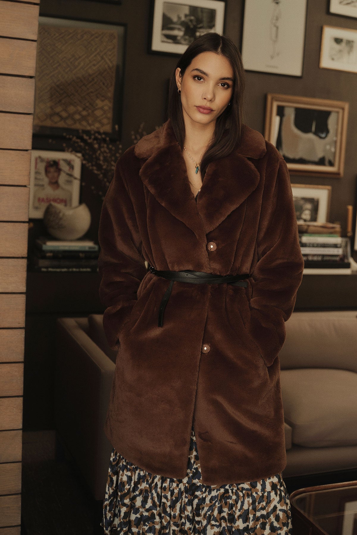   A woman in the EVALYN LUX FAUX FUR COAT by Velvet by Graham & Spencer, standing in a living room. 